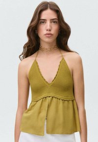 Olivovo zelený top na ramienkach s pleteným telom a splývavou, štruktúrovanou dolnou časťou, so hlbokým výstrihom do V a volánovými detailmi.