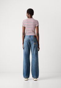 Striped red and white t-shirt paired with wide-leg blue denim jeans featuring dual back pockets and embroidered logo detail.