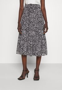 Jupe mi-longue à motif floral noir et blanc avec une taille froncée, réalisée en tissu léger, associée à des talons noirs à lanières.