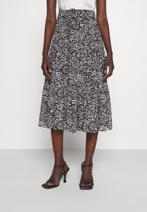 Jupe mi-longue à motif floral noir et blanc avec une taille froncée, réalisée en tissu léger, associée à des talons noirs à lanières.