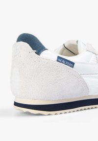 Zapatillas blancas con un talón de ante gris texturizado y un acento en azul marino. Cuenta con una suela de goma y una etiqueta "SCALPERS" en la parte trasera.