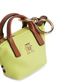 Μικρή κίτρινη τσάντα χειρός με καφέ δερμάτινες λεπτομέρειες, χρυσές μεταλλικές λεπτομέρειες, επάνω φερμουάρ και έμβλημα λογότυπου στο μπροστινό μέρος. Συμπαγής σχεδιασμός.