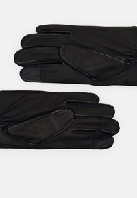 Guanti in pelle nera con cuciture bianche a contrasto, caratterizzati da una texture liscia e un design elegante, con punte delle dita parzialmente scoperte.