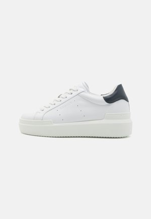 White leather sneaker with a textured sole, round toe, flat laces, and a contrasting dark blue heel tab. Prominent branding on the side.