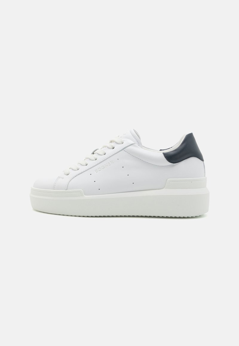 Hvit lær sneakers med teksturert såle, rund tå, flate snører og en kontrasterende mørkeblå hælflik. Fremtredende merkevare på siden.