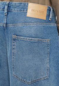 Jasnoniebieskie dżinsy z skórzaną metką marki "ONLY & SONS". Posiadają tylną kieszeń oraz kontrastowe przeszycia.