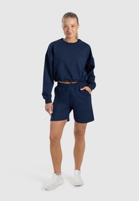 Felpa blu navy cropped e pantaloni corti coordinati realizzati in tessuto morbido, con vita elasticizzata e tasche laterali per funzionalità.