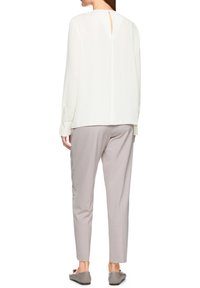 Weiße langärmlige Bluse mit einem Ausschnitt am Rücken, kombiniert mit hellgrauen, schmal zulaufenden Hosen. Minimalistisches Design und glatte Textur.