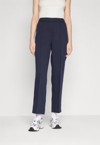 Pantalones entallados azul marino con cintura elástica, tejido suave, costuras frontales y elasticidad moderada; combinados con zapatillas blancas.