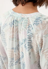 Blouse légère avec un motif floral pastel comprenant des nuances de bleu, rose et beige. Détail plissé dans le dos ajoutant de la texture.