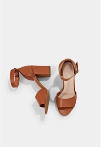 Sandales à talons hauts en cuir marron avec un talon bloc, présentant une large lanière à l'avant et une lanière de cheville avec boucle. Fini texturé, design minimal.