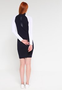 Robe marine avec de longues manches blanches et un col haut, dotée d'un détail zip noir au dos et d'une silhouette ajustée.