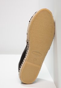 Semelle de chaussure espadrille orientée vers l'avant avec l'étiquette « Fabriqué en Espagne » et la taille 37 sur une semelle extérieure en caoutchouc beige, sur fond blanc.