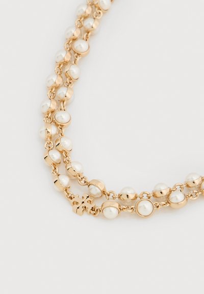 Collier en ton or avec plusieurs perles blanches rondes et des maillons circulaires, avec un petit accent logo près du fermoir.