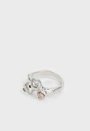 Zilveren ring met drie verschillende edelstenen: een heldere ronde, een kleine roze en een gefacetteerde heldere steen, met een gladde, afgeronde band.