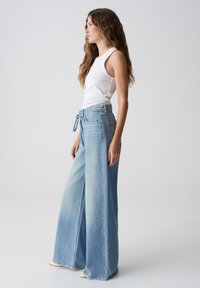 Wijd-uitlopende, lichtblauwe denim jeans met een hoge taille, strikceintuur, en twee zijzakken, gecombineerd met een aansluitend wit tanktop.