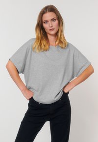 T-shirt oversize gris en tissu doux, avec des manches courtes retroussées, associé à un pantalon noir taille haute. Design simple et décontracté.