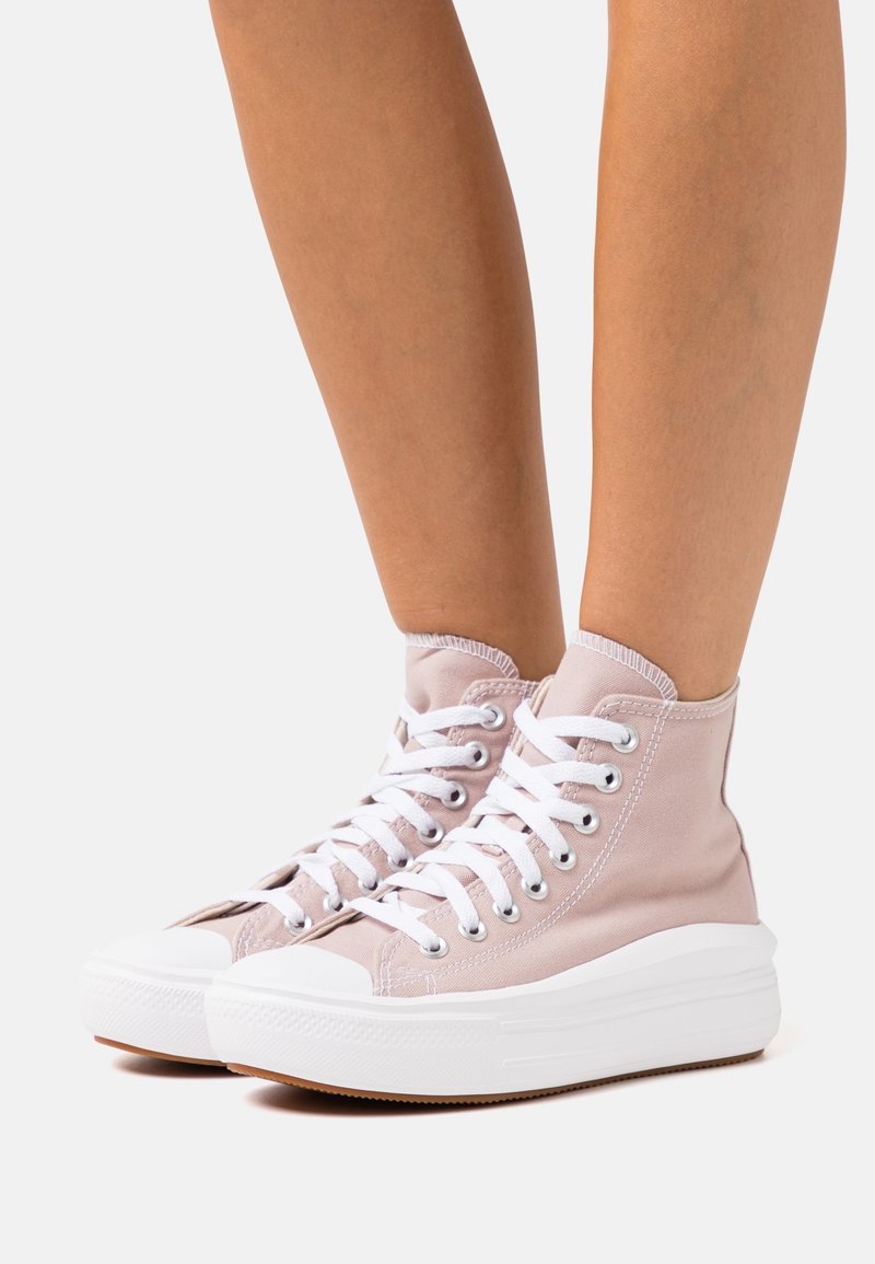 Vaaleanpunaiset korkeat tennarit kanvaamateriaalista, joissa on valkoiset nauhat, kuminen varvasrengas ja valkoinen korkea pohja. Ompeleminen silmukoiden lähellä.