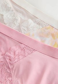 Drei Damenunterwäsche-Sets: eines cremefarben mit Spitzenbesatz, eines rosa Satin mit Spitze und eines mit Blumenmuster und glatter Textur.