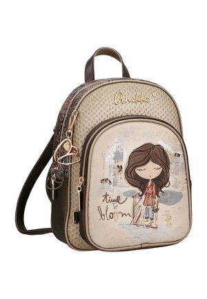 Pequeña mochila beige y marrón con una ilustración de una niña de dibujos animados, texto "time to bloom," y llavero con forma de corazón adjunto a la cremallera.