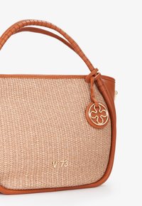 Tan handtas van gevlochten materiaal met een gladde leren afwerking en een gevlochten hengsel. Bevat een gouden bedel en een gegraveerd logo aan de voorkant.