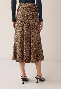 Jupe midi en imprimé léopard en tissu fluide, avec un ourlet évasé, une taille cintrée, et assortie à des talons noirs à lanières.