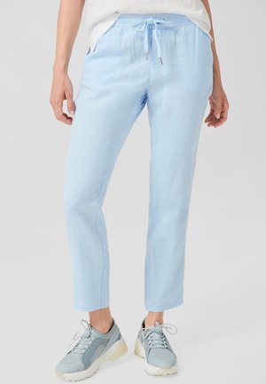 Person wearing light blue drawstring pants and gray sneakers standing on a plain background.