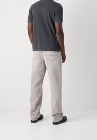 Šedé bavlněné tričko a světle šedé džíny, které mají volný střih, jednoduchý design a minimalistické detaily. Černá obuv dotváří celkový vzhled.