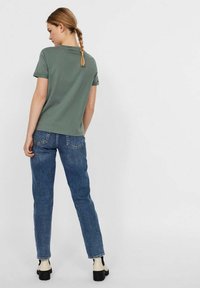 Grünes Baumwoll-T-Shirt mit kurzen Ärmeln, kombiniert mit blauen Jeans aus Denim. Das Outfit zeichnet sich durch eine lockere Passform und ein schlichtes Design aus. Schwarze Plateauschuhe.