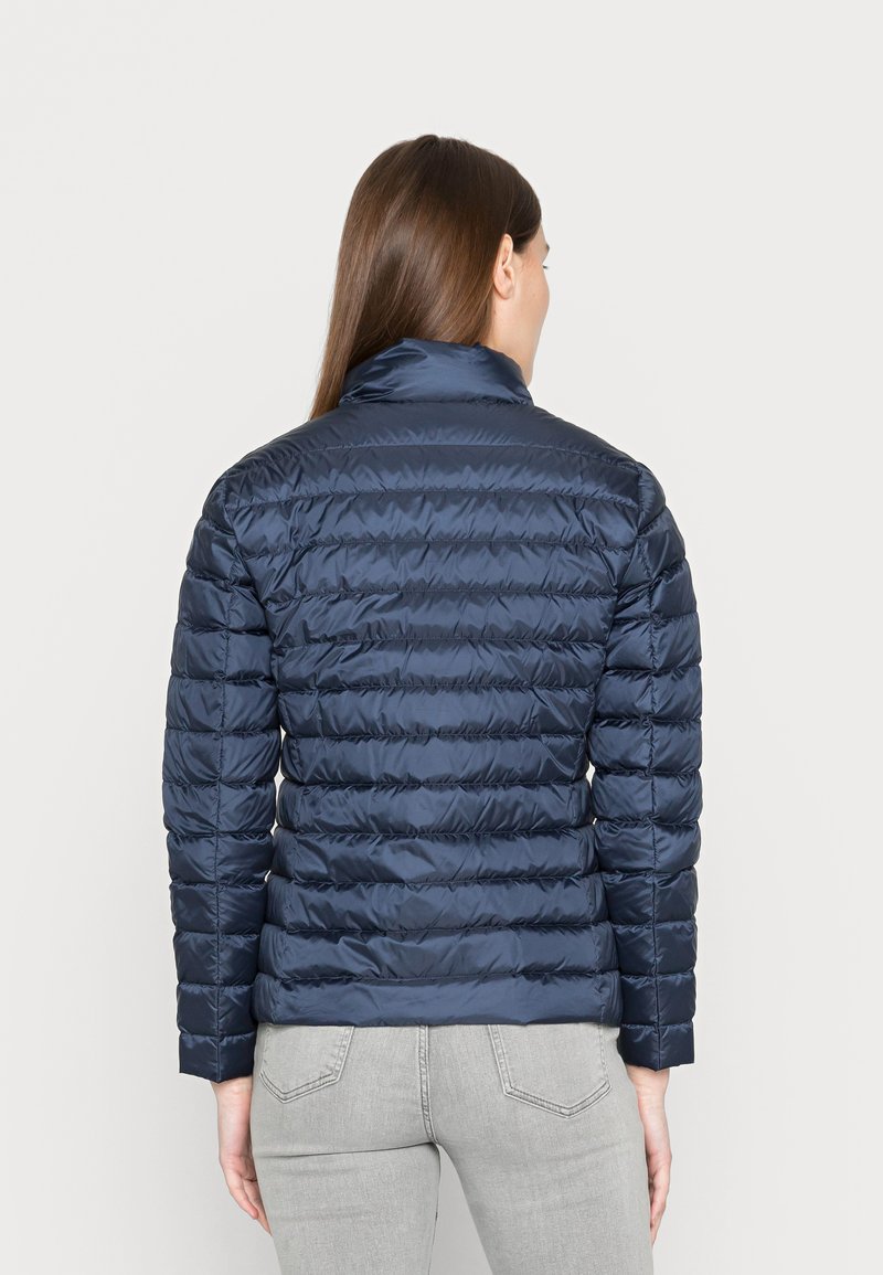 Giacca a vento blu navy con colletto alto, design trapuntato e texture lucida. Presenta maniche lunghe e una silhouette aderente.