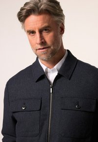 Tmavě modrá vlněná směsová bunda s límcem, předním zipem a dvěma hrudními kapsami se zapínáním na knoflíky. Texturovaná tkanina s přiléhavým střihem.