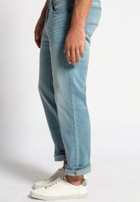 Lyseblå cowboybukser med afslappet pasform, opfoldede manchetter og minimal falmning. Sammen med hvide sneakers med grå detaljer.