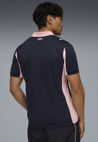 Granatowa koszulka polo z różowymi panelami po bokach, krótkimi rękawami i miękką fakturą. Posiada kołnierzyk oraz logo na karku.