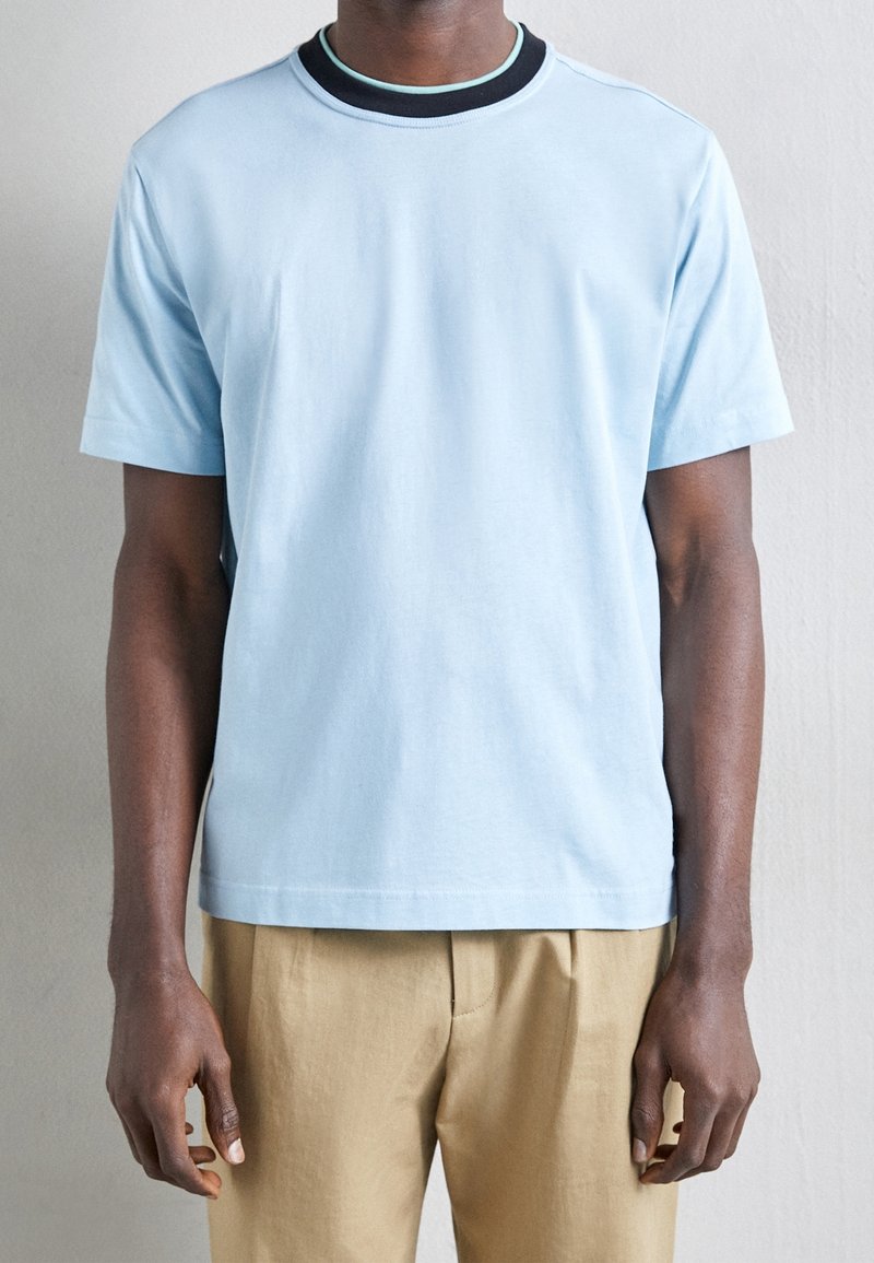 T-shirt en coton bleu clair avec un col rond, orné d'une bordure noire et turquoise. Manches courtes et coupe décontractée ; texture lisse.
