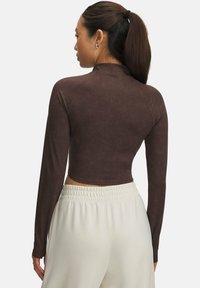 Bruine langemouwen crop top in textuurstof, met een hoge halsontwerp en naadloze details. Gecombineerd met lichtgekleurde broeken.