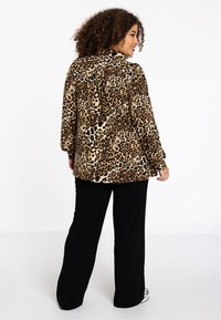 Een blouse met luipaardprint in bruin- en tan-tinten, met een kraag en lange mouwen, gecombineerd met zwarte wijde broekspijpen.