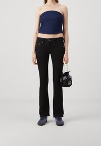 Haut sans manches bleu marine, jeans noirs ajustés, baskets grises et un sac à main noir avec un motif floral blanc et une anse ressemblant à des perles.