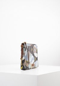 Kwiatowa torebka na ramię z wielokolorowej tkaniny, z brązowymi akcentami, zamkiem błyskawicznym i regulowanym paskiem, o gładkiej fakturze i żywym wzorze.