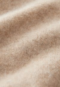Tessuto lavorato a maglia di un morbido beige con fibre sottili e una leggera texture pelosa, mostrato in dettagli ravvicinati.