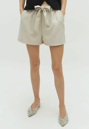 Shorts in lino crema con cintura a fusciacca, vestibilità ampia e tasche laterali. Abbinati a un top nero e ballerine a punta rigate.