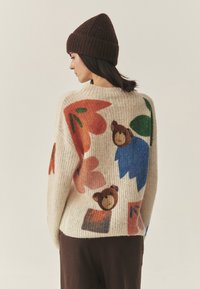 Pletena jopica z velikimi cvetličnimi in medvedjimi motivi v oranžni, modri in zeleni barvi na kremnem ozadju; mehak material; okrogla izreza in ohlapen kroj.