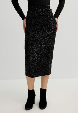 Falda midi negra con lentejuelas, cintura ajustada y abertura lateral, combinada con botas de tobillo negras de tacón. Textura suave y brillante, diseño ceñido.