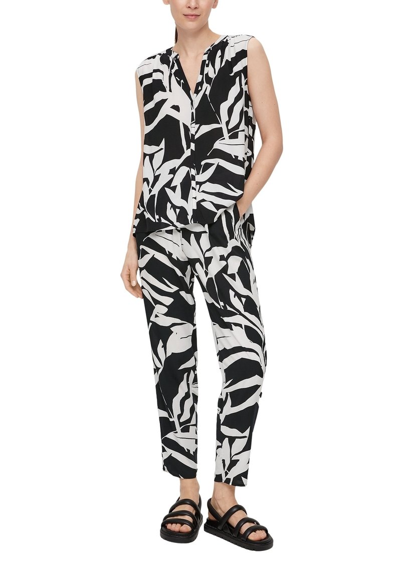 Femme portant un chemisier sans manches à motif abstrait noir et blanc et un pantalon fuselé assorti avec des sandales noires.