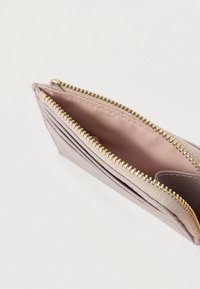 Pieni vaaleanlila lompakko, jossa on kultainen vetoketju, useita korttipaikkoja ja kangasvuorattu kolikkotasku, esitelty avoimena valkoista taustaa vasten.