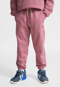 Roze joggingsbroek met elastische manchetten en een trekkoord in de taille, gecombineerd met blauwe sneakers met witte accenten en een gestructureerde afwerking.