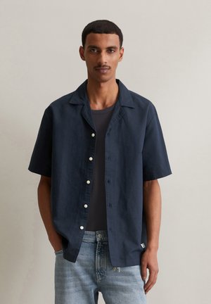 Navy blue short-sleeve shirt in lightweight fabric with a collar and button front; worn over a gray T-shirt and light wash jeans.