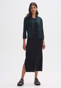 Black midi dress paired with a dark green lightweight jacket and black strappy sandals. Fabric appears smooth with a relaxed fit design.