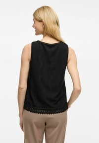 Mustata ilma varrukatop, millel on tekstuuriga laineline muster, pitsääristusega hem ja laineline kaeluse disain. Sile kangas.