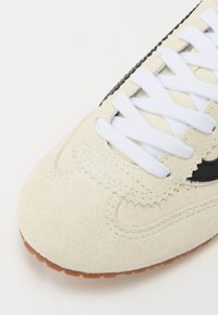 Beige Wildlederschuhe mit weißen Schnürsenkeln, schwarzen Akzenten und einer strukturierten Gummisohle. Verfügt über gebogene Nähte und ein rundes Toe-Design.