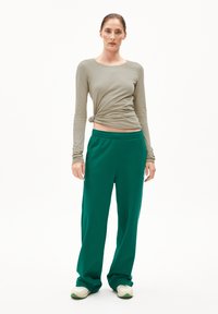 Langärmliges, helltaupefarbenes Oberteil, das an der Taille gedreht ist, kombiniert mit grünen Jogginghosen. Die Schuhe sind weiß mit grünen Akzenten. Schlichtes, entspanntes Design.